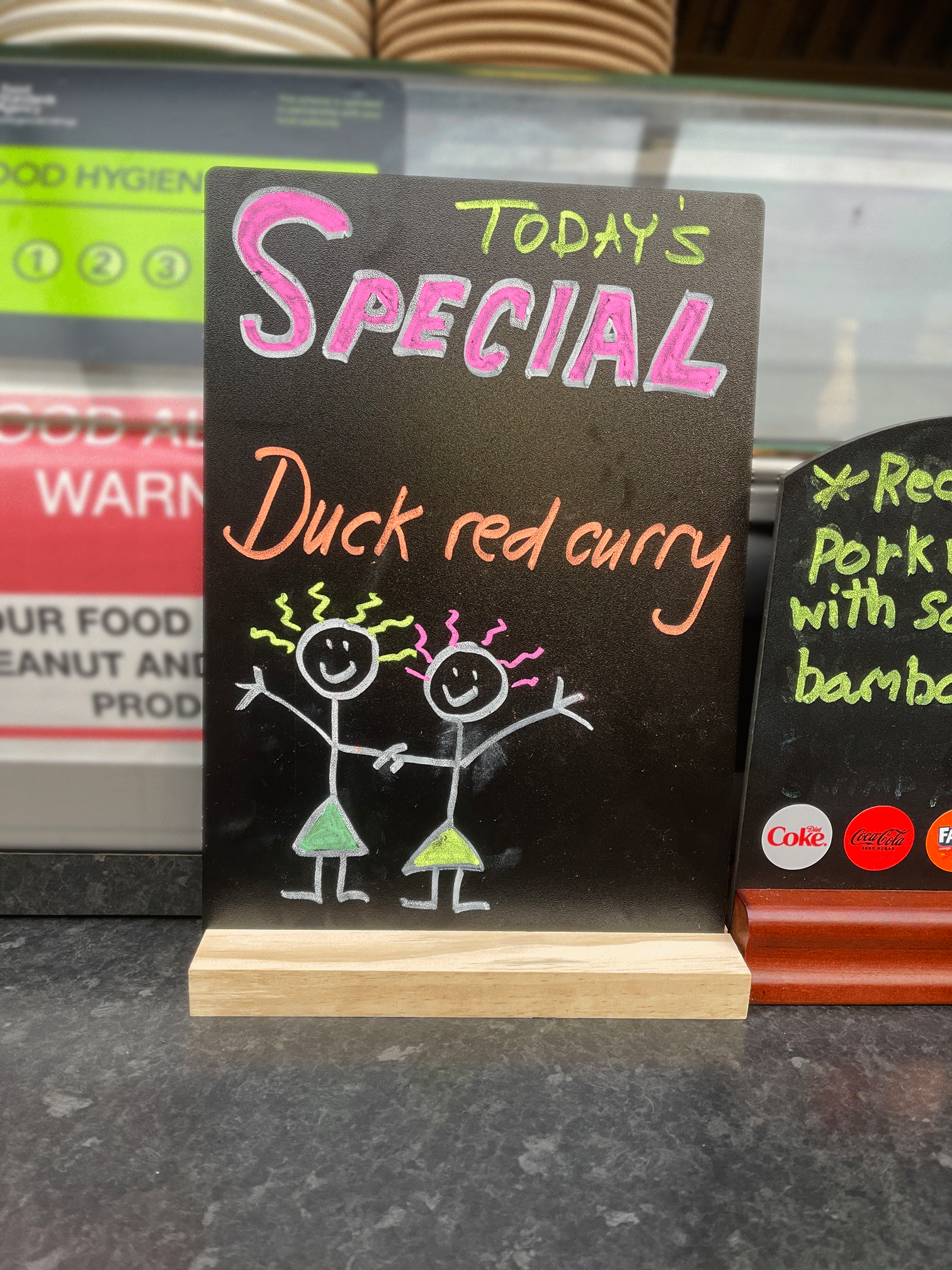 A looping animation of a sign saying Duck Red Curry with an illustration of two people with wirey, animated hair.